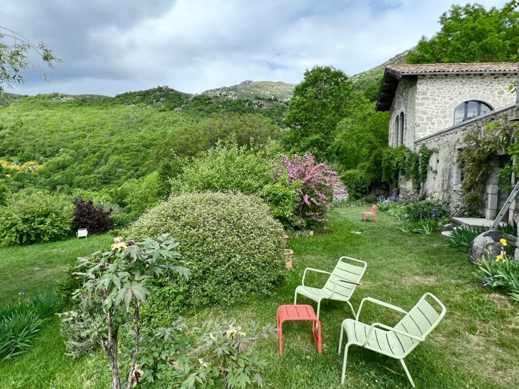 Chaises de jardin colorées devant la bâtisse en pierre et les collines